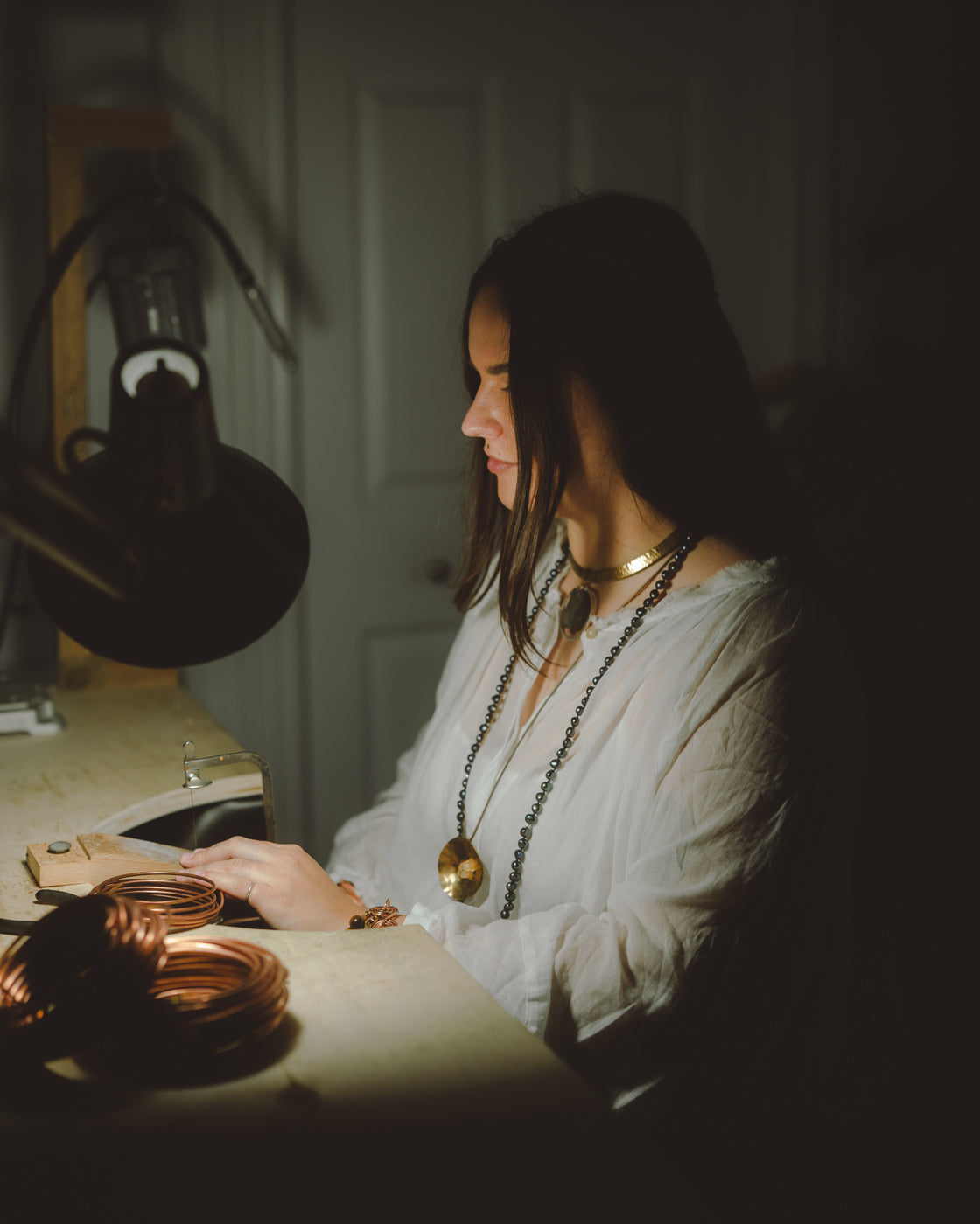 Woman sitting at a desk with jewelry, dimly lit room
