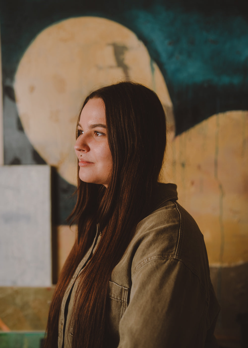 Woman with long hair wearing a green jacket in front of a colorful abstract painting