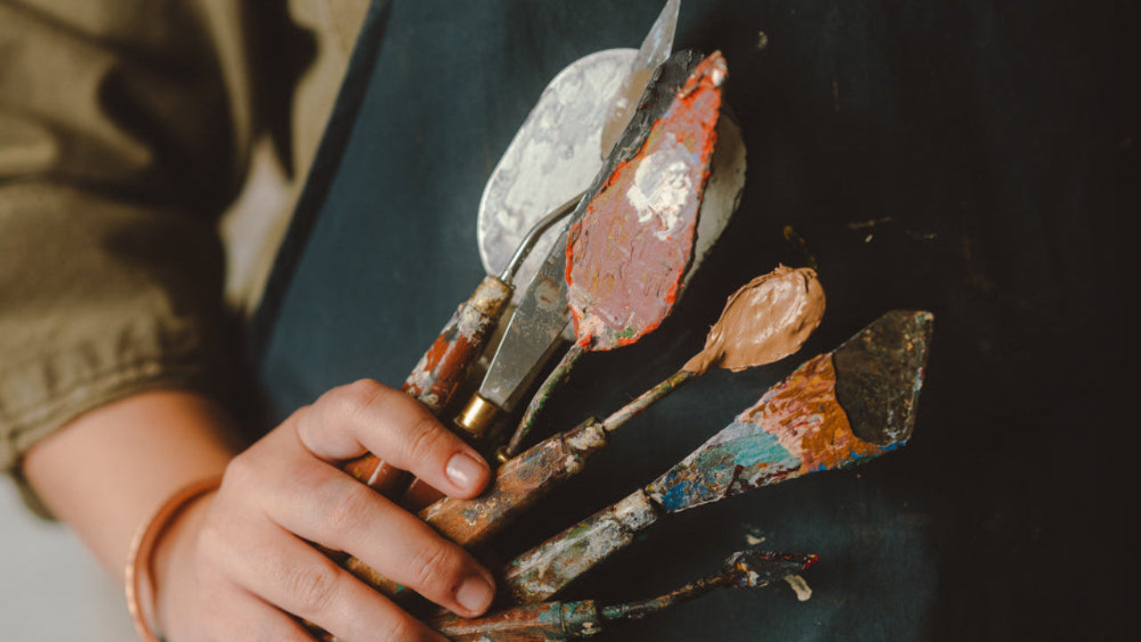 Person wearing a paint-splattered apron holding paintbrushes.