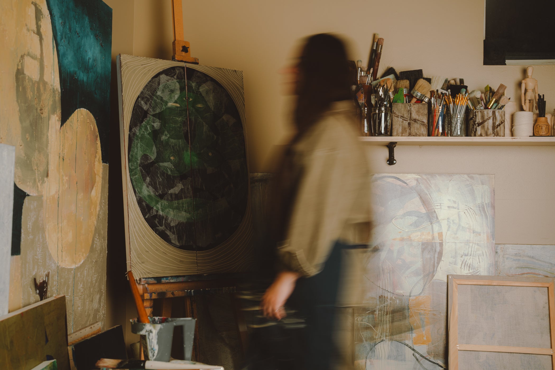 Person in an art studio with various paintings and art supplies.