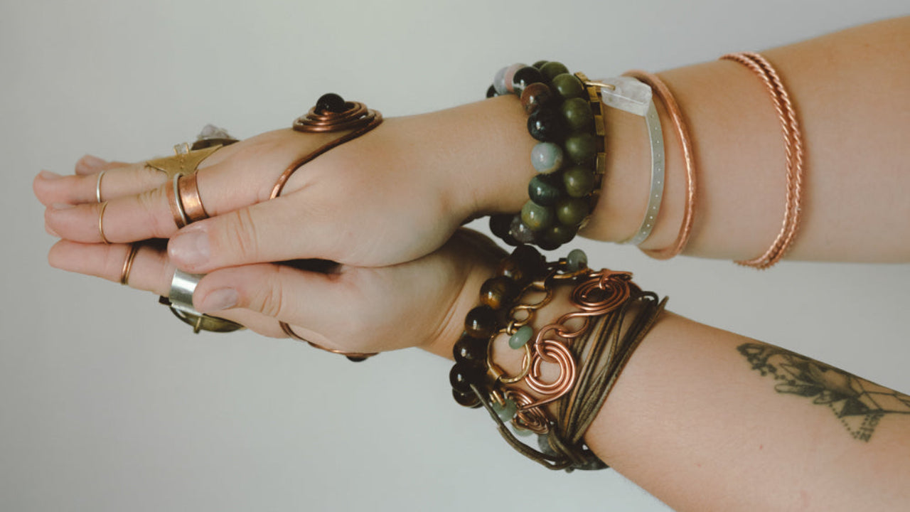 Two hands with multiple bracelets on a plain background
